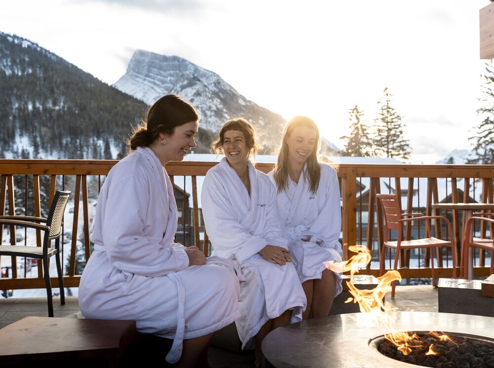 Three friends relax outside around a fire pit at the Meadow Spa at the Moose Hotel in Banff National Park.